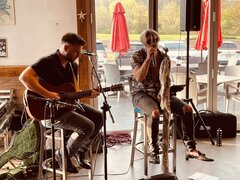 2 guys sitting on a stool playing acoustic guitar